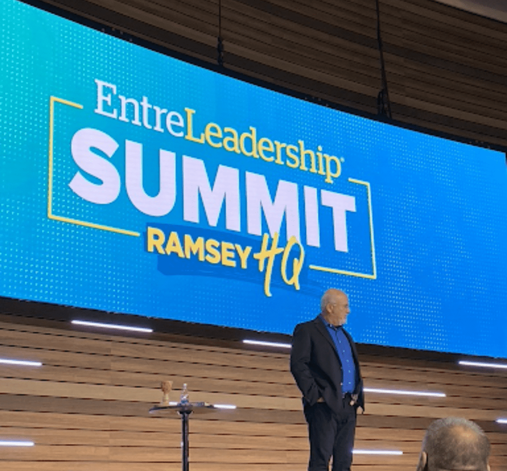 Dave Ramsey standing on stage speaking with EntreLeadership Summit on big screen behind him